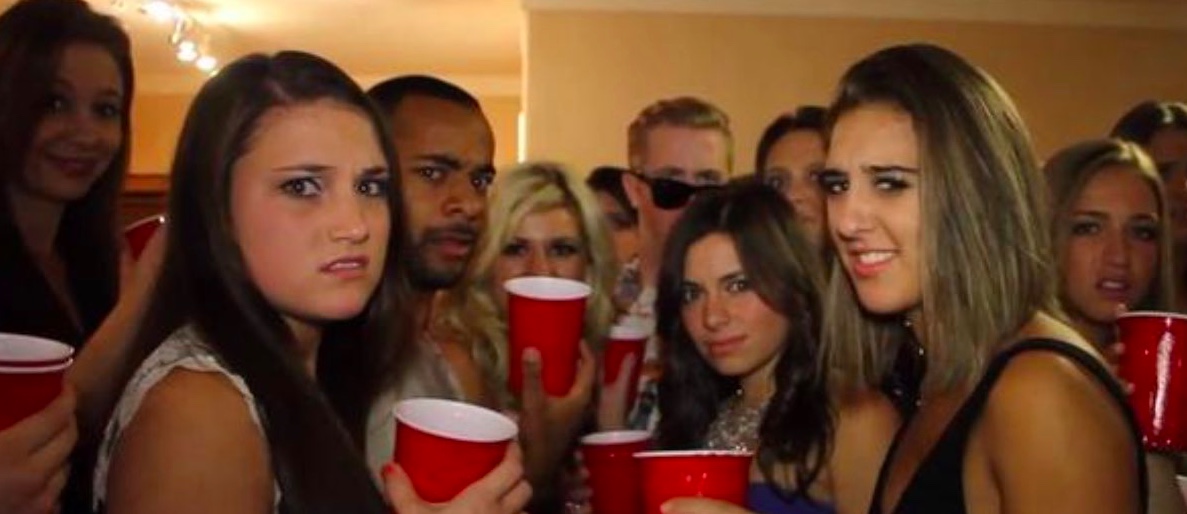 a group of college kids at a party, holding red solo cups. they are looking at the camera, each face showing emotions ranging from bemusement, confusion, to disgust.